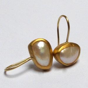 May include: A pair of gold earrings with a white pearl-like stone set in each earring. The earrings have a simple, elegant design.