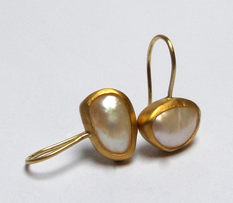 May include: A pair of gold earrings with a white pearl-like stone set in each earring. The earrings have a simple, elegant design.
