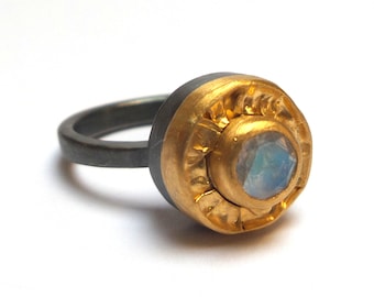 May include: A silver ring with a gold band and a round, iridescent gemstone.