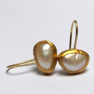 May include: A pair of gold earrings with a white pearl in each. The earrings are made of a smooth, rounded metal and have a simple, elegant design.