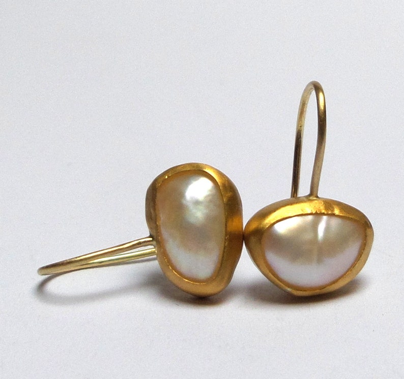 May include: A pair of gold earrings with a white pearl in each. The earrings are made of a smooth, rounded metal and have a simple, elegant design.
