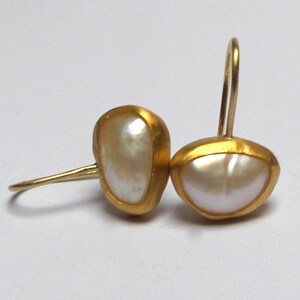 May include: A pair of gold earrings with white pearl accents. The earrings are shaped like a teardrop and have a simple, elegant design.