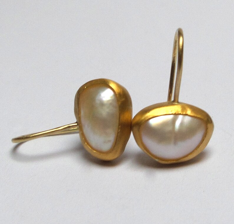 May include: A pair of gold earrings with white pearl accents. The earrings are shaped like a teardrop and have a simple, elegant design.