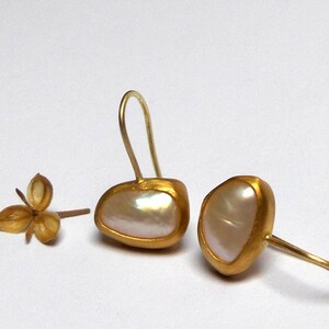 May include: A pair of gold earrings with white pearl-like stones. The earrings have a simple, elegant design.
