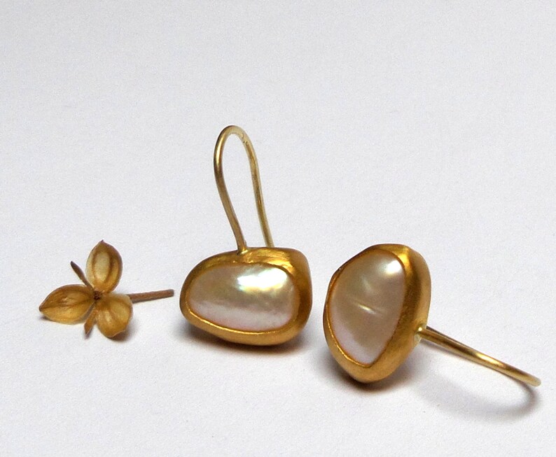 May include: A pair of gold earrings with white pearl-like stones. The earrings have a simple, elegant design.