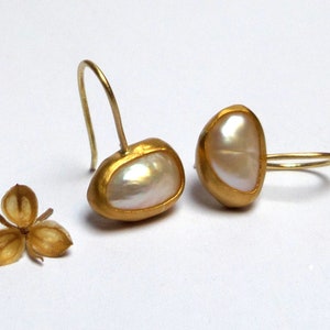 May include: A pair of gold earrings with a white pearl-like stone set in each. The earrings have a simple, elegant design.
