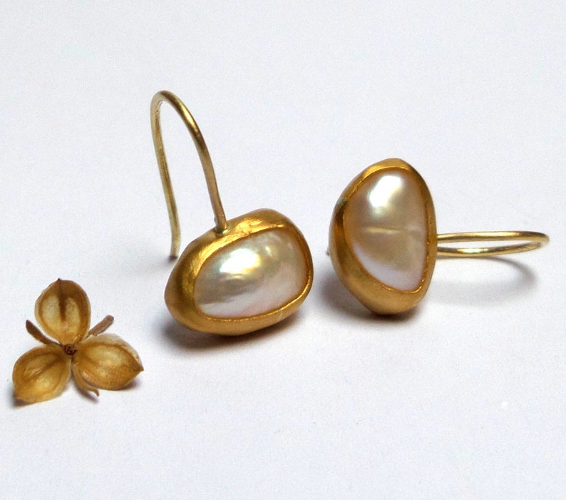 May include: A pair of gold earrings with a white pearl-like stone set in each. The earrings have a simple, elegant design.