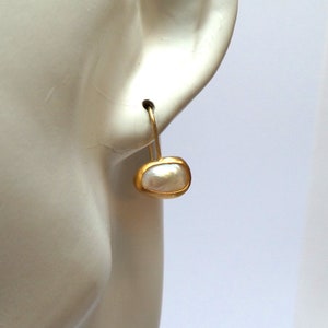 May include: A pair of gold earrings with a white pearl in a gold setting. The earrings are shown on a mannequin's ear.