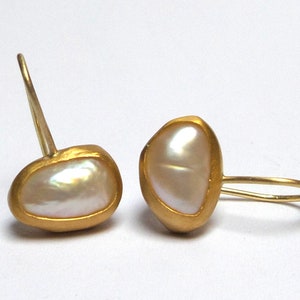 May include: A pair of gold earrings with a white pearl in each. The pearls are set in a gold frame and the earrings have a simple hook closure.