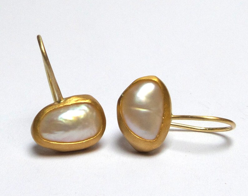 May include: A pair of gold earrings with a white pearl in each. The pearls are set in a gold frame and the earrings have a simple hook closure.