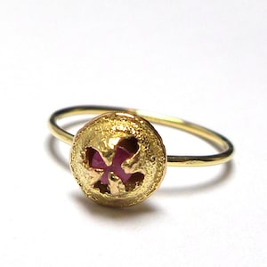 Pode incluir: Um anel de ouro com uma banda texturizada e uma gema rosa engastada em um design em forma de flor.