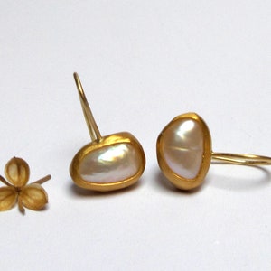 May include: A pair of gold earrings with a white pearl in each. The pearls are set in a gold frame and the earrings have a simple hook closure.