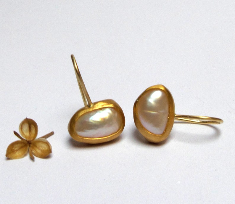 May include: A pair of gold earrings with a white pearl in each. The pearls are set in a gold frame and the earrings have a simple hook closure.