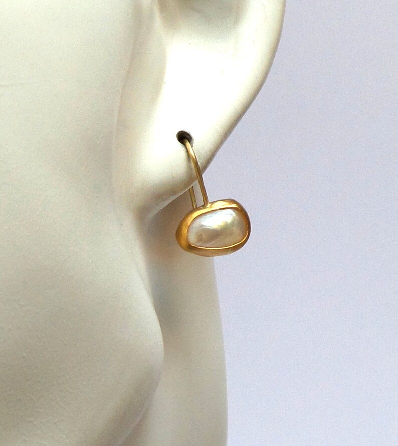 May include: Gold hoop earrings with a white pearl drop. The pearl is set in a gold bezel.