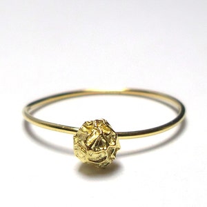 Pode incluir: Um delicado anel de ouro com um design esférico texturizado. O anel tem uma banda fina e polida que leva ao ponto focal: um orbe dourado detalhado. O anel está sobre um fundo branco liso, destacando seu design intrincado.