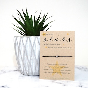 May include: A brown card with black text that reads "Friends are like stars. You don't always see them, but you know they're always there."  A black string bracelet with a white star charm is attached to the card. The card also has the text "As you tie this on your wrist, close your eyes and make a wish. Once the dainty thread wears through, then your wish may soon come true! tealawletudio.etsy.com"