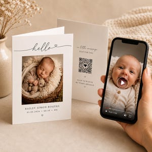 May include: A white baby announcement card with the word "hello" in script. The card features a photo of a sleeping baby with a teddy bear. The card also includes the baby's name, date, time, and weight. A phone displays a video of the baby.