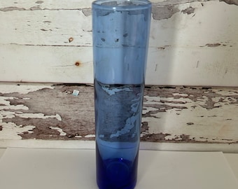 May include: A tall, clear glass vase with a blue ombre effect. The vase is cylindrical and has a rounded bottom.