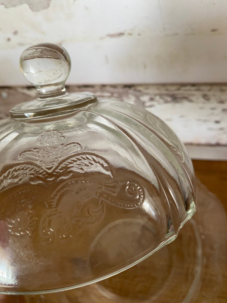Peut inclure: Cloche en verre transparent avec un motif floral d&eacute;coratif. La cloche a un bouton sur le dessus et une forme de d&ocirc;me arrondie.