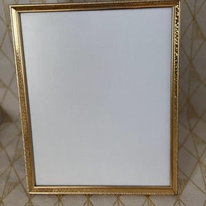 May include: A rectangular picture frame with a metallic gold finish and a textured, beaded border. The frame features a plain white mat board insert, providing a clean and neutral display area for a photograph or artwork of choice.