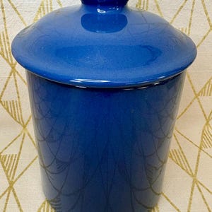 May include: A cobalt blue ceramic canister with a matching lid. The cylindrical container has a glossy finish and a decorative pattern. The lid has a knob for easy removal. This kitchen storage item is suitable for dry goods.