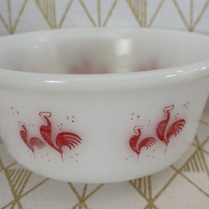 May include: White ceramic bowl with a red rooster design. The bowl has a rounded shape and a smooth, glossy finish. The rooster design is repeated around the bowl's exterior, adding a touch of vintage charm. A classic piece for serving or display.