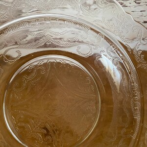 Peut inclure: Une assiette en verre transparent avec un bord festonn&eacute; et un motif grav&eacute; complexe de feuilles et de vignes tourbillonnantes. L'assiette a une teinte l&eacute;g&egrave;rement ambr&eacute;e.