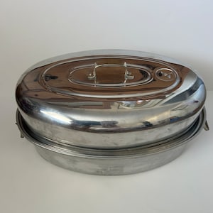 May include: A silver oval-shaped roasting pan with a lid and two handles. The pan is made of metal and has a shiny finish.