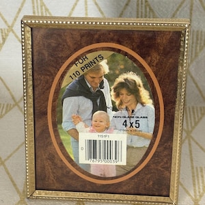 May include: A rectangular picture frame with a gold-toned beaded border and a faux wood grain finish. The frame contains a display insert with the text FOR 110 PRINTS, NON-GLARE GLASS, 4x5 (10cm x 13cm), and a barcode with the number 0 76795 00039.