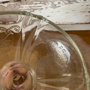 Peut inclure: Un support &agrave; g&acirc;teau en verre transparent avec un bord festonn&eacute; et un motif floral. Le support a un pi&eacute;destal central avec une base ronde.