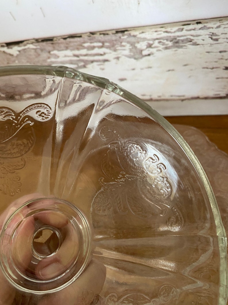 Peut inclure: Un support &agrave; g&acirc;teau en verre transparent avec un bord festonn&eacute; et un motif floral. Le support a un pi&eacute;destal central avec une base ronde.