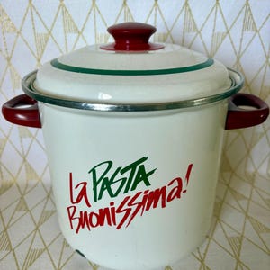 May include: A white enamel pasta pot with a matching lid, featuring red side handles and a red lid knob. The pot displays the green and red text "la PASTA BUONISSIMA!" on the front, with a thin green stripe encircling the lid and a silver rim.
