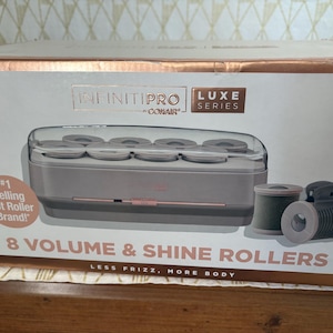 May include: A rectangular product box for the Infinitipro by Conair Luxe Series 8 Volume & Shine Rollers. The box features a gray and rose gold color scheme, displaying the hot roller heating unit and two individual hair rollers.