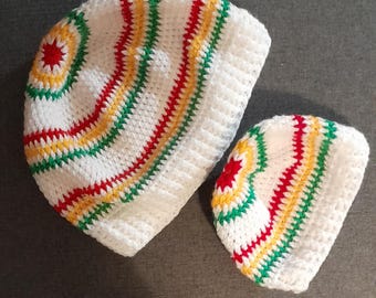 Puede incluir: Dos gorros de ganchillo blancos con rayas rojas, amarillas y verdes. El gorro más grande es ligeramente más grande que el más pequeño.
