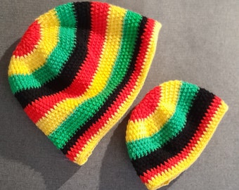 Puede incluir: Dos gorros de ganchillo con un patrón de rayas rojas, amarillas, verdes y negras. El gorro más grande es ligeramente más grande que el más pequeño.