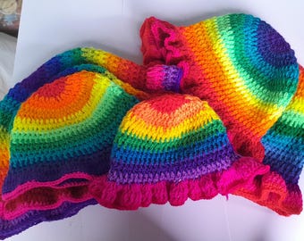 Puede incluir: Dos sombreros de pescador de ganchillo con un vibrante patrón de degradado de arcoíris. Cada sombrero está construido con una corona circular y un ala ancha con volantes. El hilo transita por tonos rojos, naranjas, amarillos, verdes, azules y morados.