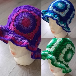 Op de afbeelding: Drie kleurrijke gehaakte emmerhoeden. Eén is paars, roze en magenta. Een andere is blauw, turquoise en wit. De derde is groen en wit. Elke hoed heeft een cirkelvormig patroon en een gerimpelde rand.