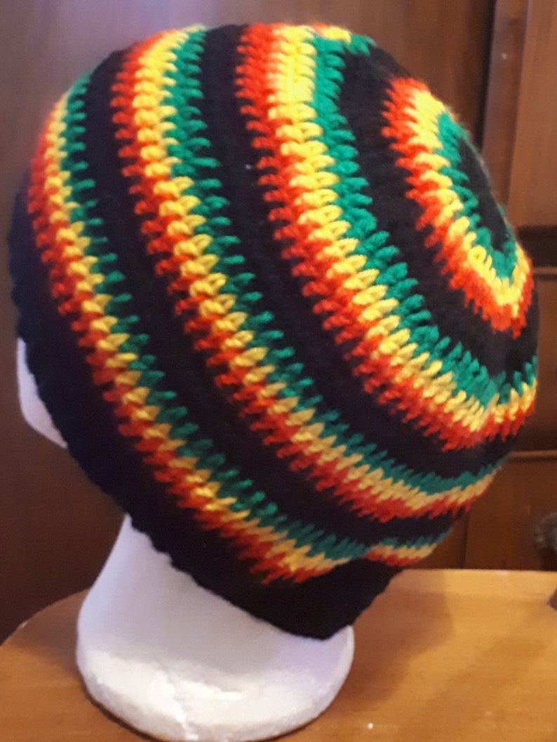Puede incluir: Un gorro de punto de color negro, verde, rojo y amarillo. El gorro est&aacute; hecho con un patr&oacute;n en espiral.