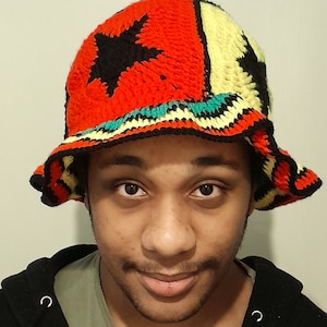 May include: A person wearing a red, yellow, green, and black crocheted bucket hat with a black star design.
