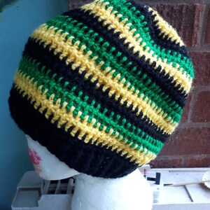 Puede incluir: Un gorro de punto de rayas negras, verdes y amarillas. El gorro est&aacute; en una cabeza de poliestireno blanco.
