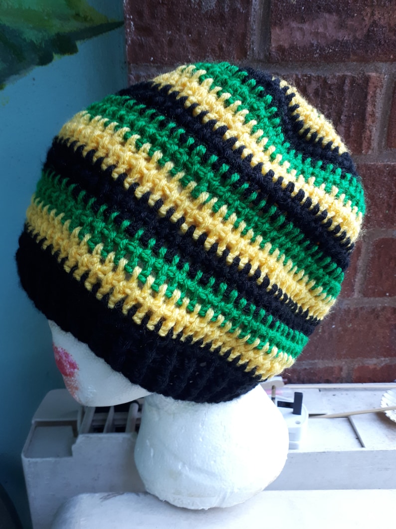 Puede incluir: Un gorro de punto de rayas negras, verdes y amarillas. El gorro est&aacute; en una cabeza de poliestireno blanco.