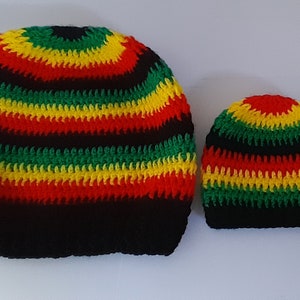 Puede incluir: Dos gorros de ganchillo en rayas negras, rojas, amarillas y verdes. El gorro m&aacute;s grande est&aacute; a la izquierda y el m&aacute;s peque&ntilde;o a la derecha.