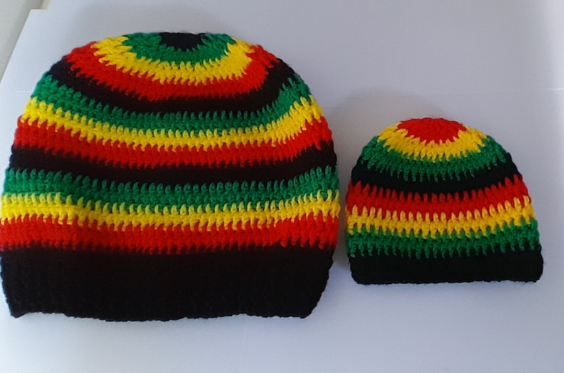 Puede incluir: Dos gorros de ganchillo en rayas negras, rojas, amarillas y verdes. El gorro m&aacute;s grande est&aacute; a la izquierda y el m&aacute;s peque&ntilde;o a la derecha.