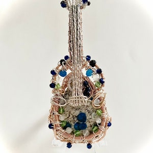 May include: A wire-wrapped guitar pendant featuring a stone inlay and blue, green, and white beads.