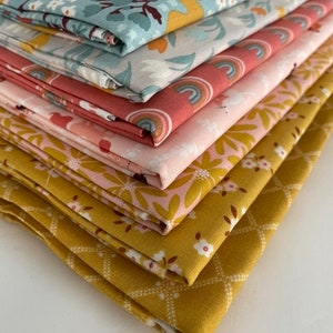 May include: A stack of six fabric squares in various patterns. The top fabric is a light blue with a floral pattern and rainbows. The second fabric is a light gray with a floral pattern. The third fabric is a pink with a rainbow pattern. The fourth fabric is a light pink with a floral pattern. The fifth fabric is a yellow with a floral pattern. The bottom fabric is a yellow with a diamond pattern.