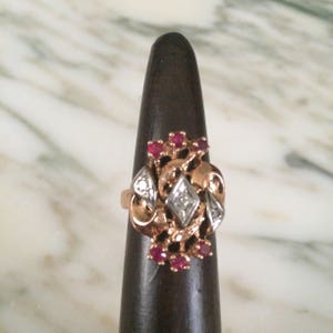 Puede incluir: Un anillo de oro con un diamante grande y claro en el centro y diamantes más pequeños y rubíes rojos que lo rodean.