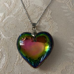 May include: A silver chain necklace with a iridescent heart-shaped pendant. The pendant is made of glass and has a rainbow of colors.