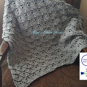 Può includere: Una coperta di uncinetto grigia con un bordo a scalare. La coperta è drappeggiata su una sedia di legno. Il testo "Gigi's Blue Rose" è ricamato sulla coperta.