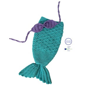 以下が含まれることがあります： ターコイズブルーのクロシェ編みの人魚姫の尻尾とパープルのクロシェ編みのヘッドバンド。尻尾は赤ちゃんまたは幼児向けにデザインされており、波打つ縁取りがあります。ヘッドバンドは長い紐で結ばれています。画像には「Crochet Pattern Gigi's Blue Rose」というテキストが含まれています。