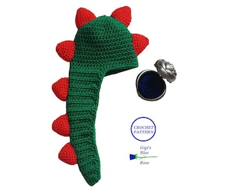 May include: Green and red crocheted dinosaur hat with a long tail. The hat is designed for a baby or toddler. The hat is on a white background. The text "Crochet Pattern" is in a circle with a blue background. The text "Gigi's Blue Rose" is below the circle.